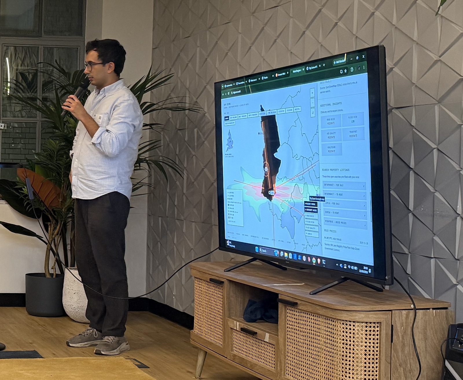 Bilal Khizar speaking into a microphone beside a large screen showing the Sky Score map of London's flight paths.